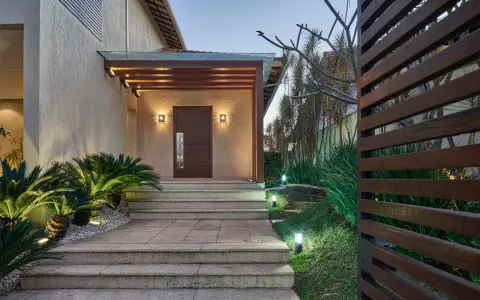 Un portico moderno con porta in legno scuro, illuminazione soffusa e piante rigogliose. Un esempio di come abbellire un portico con stile e natura.