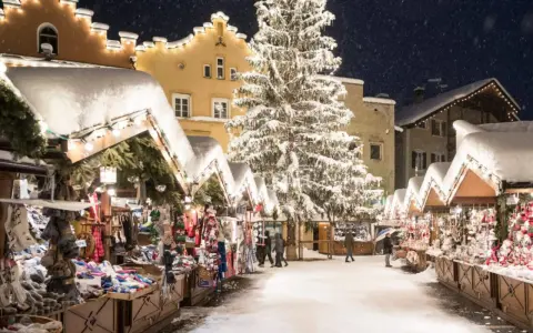 Mercatini di Natale nel Nord Italia, con bancarelle innevate, un grande albero illuminato e case decorate. Magia invernale.