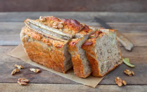Pyszny chlebek bananowy z bakaliami, pokrojony w kromki, z widocznymi orzechami i bananem na wierzchu.