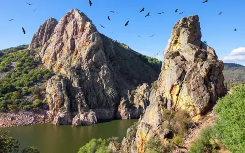 Felsige Berge und ein Fluss in Extremadura, Spanien. Geier kreisen am blauen Himmel über der rauen Landschaft.