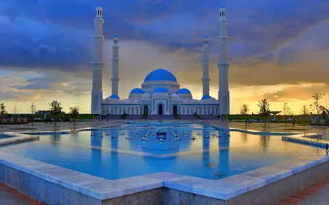 Die Hazrat-Sultan-Moschee in Astana, ein architektonisches Meisterwerk, spiegelt sich im Wasser eines Brunnens unter einem dramatischen Abendhimmel.