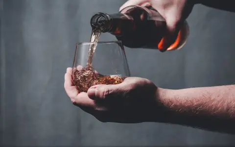 Dłoń nalewa bursztynowy płyn z butelki do szklanki. Czy whisky to bimber?