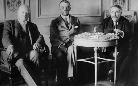 Tres hombres sentados, discutiendo los términos del **Tratado de Locarno**. Uno de ellos, a la derecha, manipula documentos sobre una mesa.