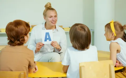 Nauczycielka pokazuje literę "A" grupie dzieci. Jedno z dzieci, 6-latek, uważnie słucha.