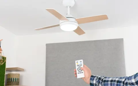 Mano con mando a distancia operando un ventilador de techo escayola con luz integrada.