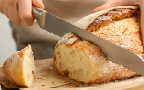 Krojenie świeżo upieczonego bochenka, idealnego na domowy przepis na chleb pieczony w piekarniku. Chrupiąca skórka i miękki środek.