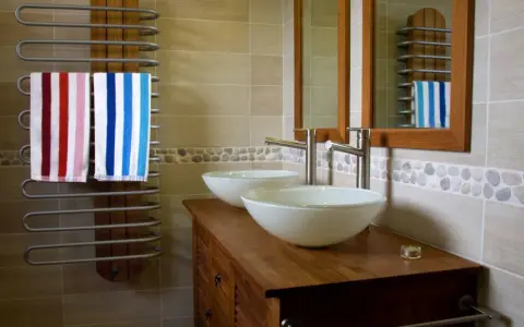 Salle de bain moderne avec double vasque. L'arrivée d'eau est discrète, deux lavabos blancs reposent sur un meuble en bois. Deux serviettes rayées sèchent sur un radiateur.