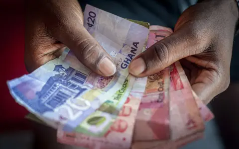 Dłonie trzymające banknoty cedi Ghany o różnych nominałach.