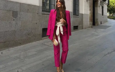 Mujer sonriente luce un espectacular outfit rosa de traje pantalón y blazer, con un cinturón blanco y bolso a juego.