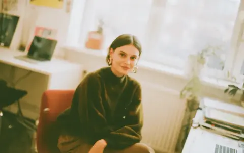 Młoda kobieta w zielonym swetrze siedzi przy biurku, przygotowując się do zajęć z architektura studia zaoczne.
