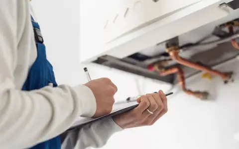 Technik w niebieskim kombinezonie notuje wyniki przeglądu kominiarskiego, który powinien być wykonywany co najmniej raz w roku.