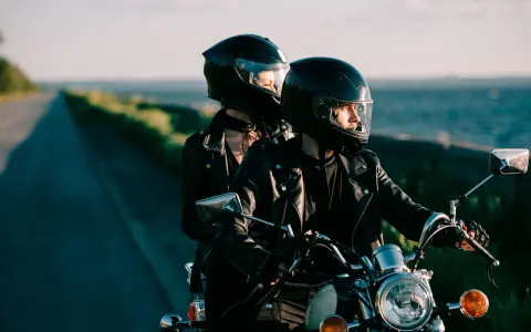 Coppia in moto romantica, con caschi neri, giacche di pelle, su una strada panoramica al tramonto.