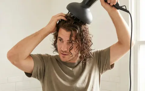 Ein junger Mann mit wellen haaren föhnt sich die Locken mit einem Diffusor.
