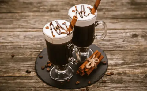 Dwa Irish coffee z bitą śmietaną, polewą czekoladową i laską cynamonu. Jaki to smak? Słodki, kawowy, z nutą alkoholu i przypraw.