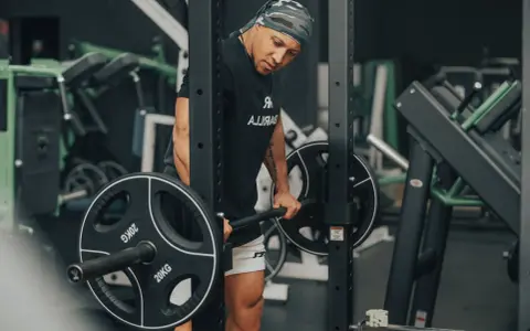 Mann im Fitnessstudio bereitet sich auf schwere myo reps vor, hält eine Langhantel mit 20kg Scheiben.