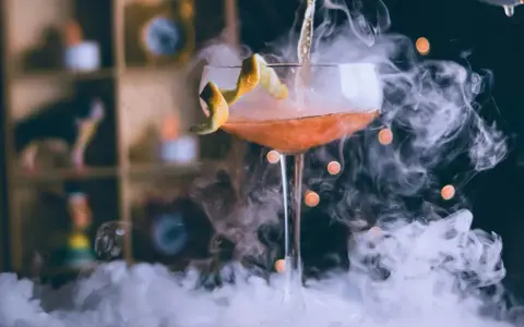 Dymiący drink przepis: koktajl w kieliszku z pomarańczową skórką, otoczony mgłą.
