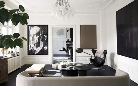 Ett elegant vardagsrum för ett hemma hos reportage. En stor porträttbild, en svart fåtölj och en rund soffa skapar en lyxig atmosfär.