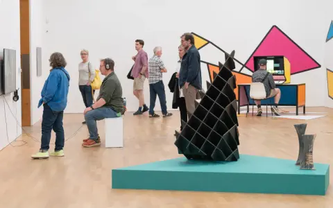 Visitors explore diverse artworks in what is an art gallery, from video installations to abstract sculptures and colorful wall art.