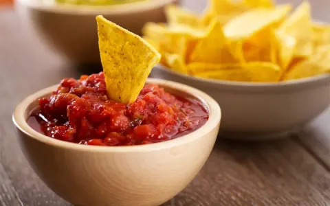 Una tortilla croccante affonda in una ciotola di fresca salsa messicana per tortillas, con altre tortillas sullo sfondo.