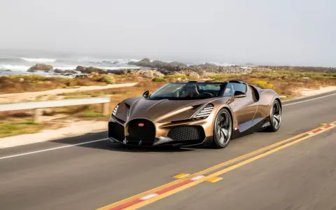 Ein bronzener Bugatti Mistral fährt auf einer Küstenstraße.
