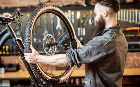 Mechanik z brodą sprawdza oponę gravelową roweru. Zastanawia się, ile mleka do opony gravel będzie potrzebne, by zapewnić najlepszą przyczepność.
