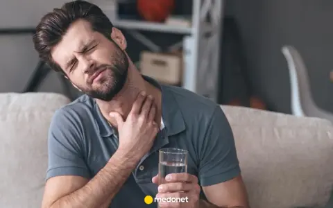 Mężczyzna z bólem gardła, trzymający szklankę wody, szuka sposobu, jak pozbyć się drapania w gardle.