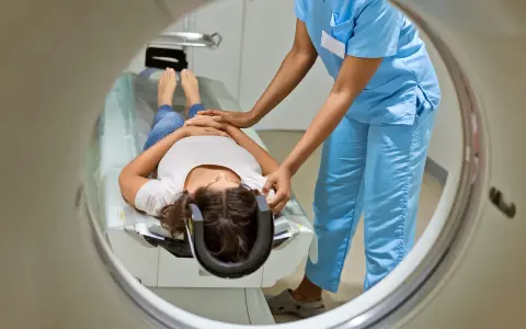 Eine Patientin liegt für eine MRT Untersuchung auf einer Liege, während eine medizinische Fachkraft sie vorbereitet.