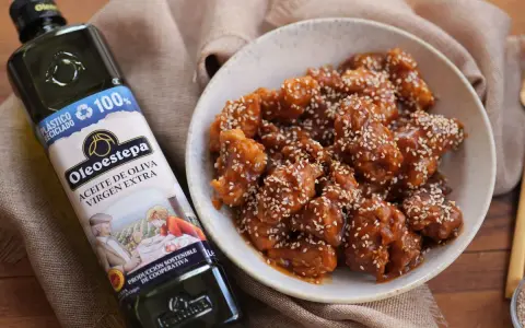 Delicioso pollo agridulce cubierto de semillas de sésamo en un cuenco, junto a una botella de aceite de oliva virgen extra Oleoestepa.