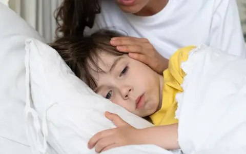 Chore dziecko w łóżku, mama głaszcze je po czole. Warto pamiętać o odpowiednich paracetamol czopki dawki dla dzieci.
