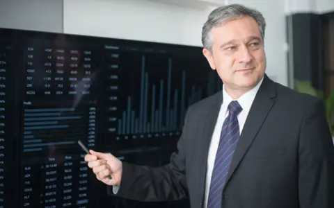 Mężczyzna w garniturze wskazuje na ekran z danymi finansowymi, wyjaśniając, kto płaci doradcy kredytowemu.