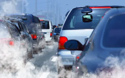 Tráfico denso con humo saliendo de los coches, reflejando la contaminación.