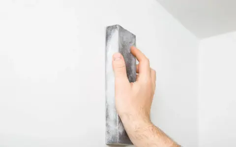 Mano lijando una pared blanca para reparar grietas en techo de yeso.