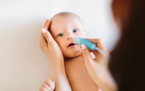 Mama delikatnie oczyszcza nosek niemowlaka z katarem za pomocą aspiratora.