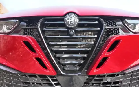 Czerwona Alfa Romeo z bliska. Widoczny grill w kształcie tarczy z logo, reflektory i detale karoserii w zbliżeniu. Alfa makro.