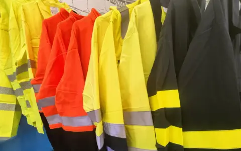 Variedad de ropa de alta visibilidad normativa en colores amarillo, naranja y negro, con bandas reflectantes para garantizar la seguridad en entornos de trabajo.