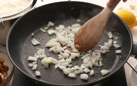 Cebolla picada se sofríe en una sartén, parte de unas deliciosas recetas con cebolla. Arroz blanco y mariscos esperan.
