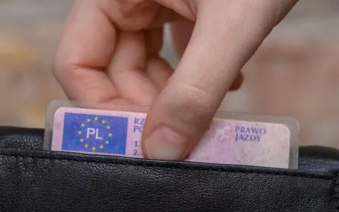 Dłoń wyjmuje z czarnego portfela polskie prawo jazdy.