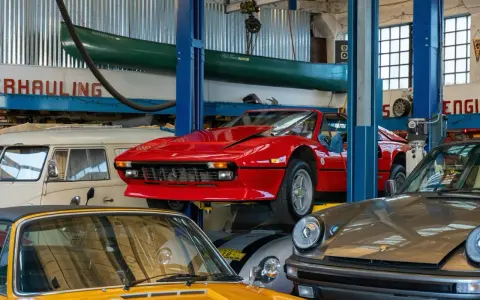Taller mecánico con autos clásicos: un rojo Ferrari en elevador, un Porsche gris y un amarillo. ¡Ideas para tu taller!