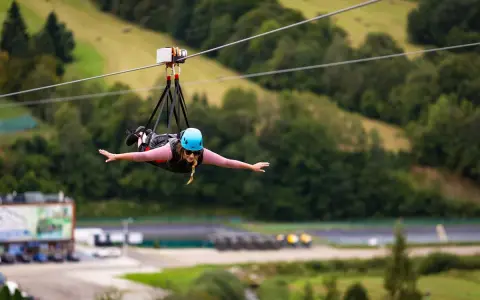 Kobieta w kasku leci na tyrolce, doświadczając adrenaliny na najdłuższej tyrolce w Polsce.