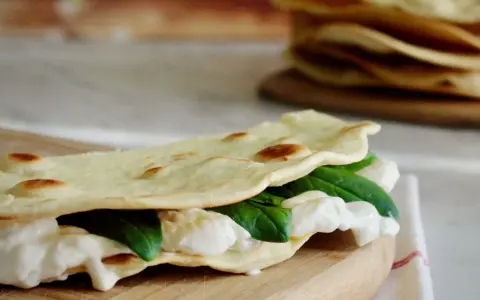 Piadina fatta in casa ripiena di mozzarella filante e spinacini freschi, pronta per essere gustata.
