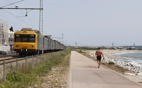 Gelber Zug fährt entlang der Küste von Cascais nach Lissabon. Ein Mann joggt am Strand entlang.