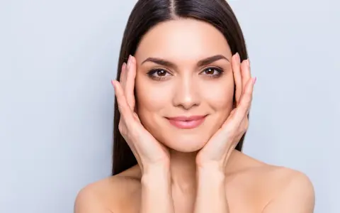 Mujer con piel radiante, resultado del colágeno para la piel. Sus manos acarician su rostro, mostrando una tez suave y luminosa.