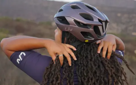Donna con dreadlocks che regola un casco da bici Liv. Non preoccuparti se il tuo casco è stretto, ci sono modi per allargare il casco stretto.