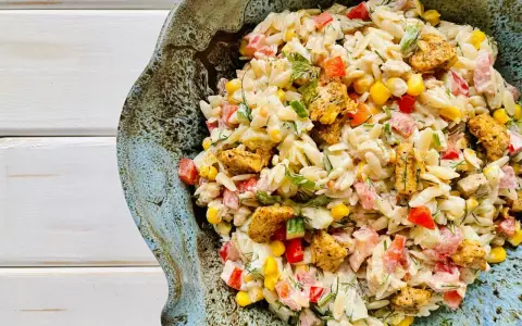 Pyszna sałatka z makaronem orzo i kurczakiem, z dodatkiem kukurydzy, papryki i ziół, podana w ceramicznej misie.