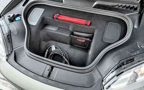 Otwarty bagażnik Porsche Macan z kablem do ładowania, apteczką i instrukcją.