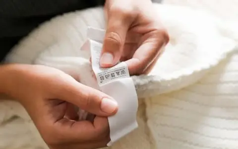 Dłonie trzymają białą metkę z symbolami pielęgnacji. To oryginalna metka Off-White, która informuje o sposobie prania swetra.