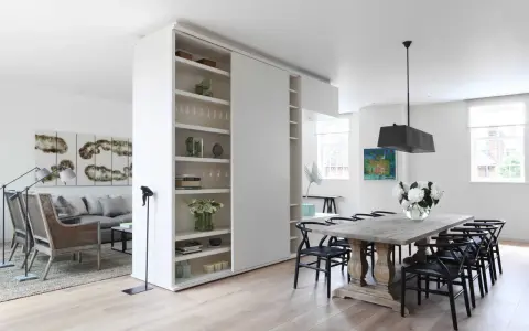 En vit rumsavdelare etta med hyllor delar av ett modernt vardagsrum och matplats.