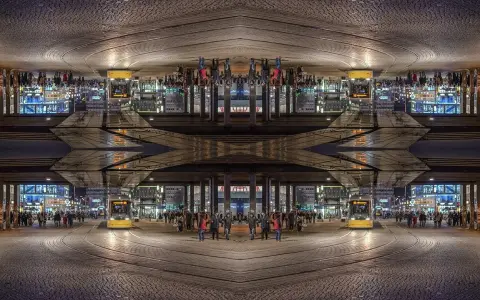 Nocne miasto z żółtym tramwajem i ludźmi. Kompozycja symetryczna tworzy surrealistyczny, odbity świat.