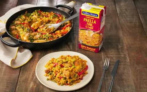 Paella de carne recién hecha en sartén y plato, lista para disfrutar. Un caldo Gallina Blanca para paella fácil de carne a su lado.
