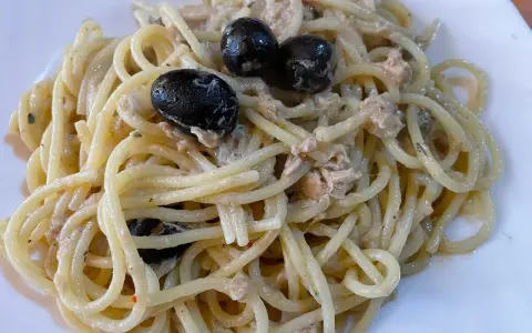 Un piatto di spaghetti conditi con tonno e olive nere, un classico della cucina italiana.